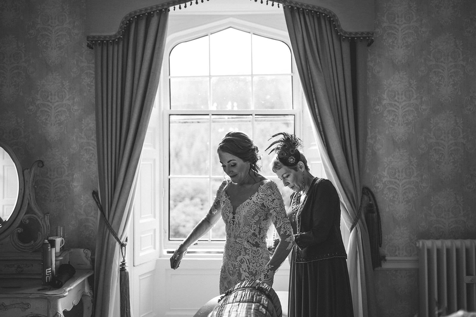 Bride and attendant arranging a lace wedding dress beside a castle window