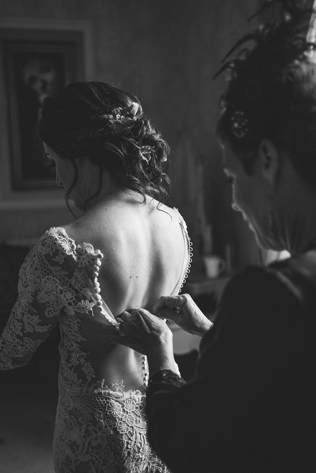 Attendant fastening the back of the bride's lace wedding dress